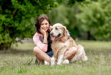 Golden retriever köpeği olan güzel bir kız doğada oturuyor. Yazın parkta safkan evcil köpek labrador 'una sarılan güzel bir genç kadın.