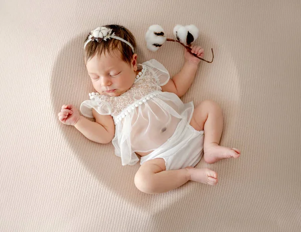 stock image Adorable newborn baby girl in white dress and wreath sleeping in heart shape form with cotton flower. Cute infant child kid napping