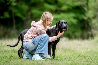 Golden Retriever köpeğini kucaklayan küçük kız doğada birlikte oturuyor. Sevimli çocuk yazın parkta safkan köpek labrador 'u besliyor.