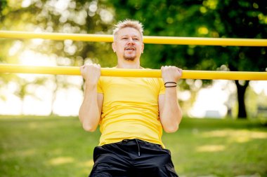 Sağlıklı bir yaşam için parkta barfiks çeken bir adam. Sporcu adam kas için sıkı çalışıyor.