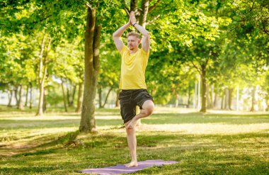 Yazın tek ayak üstünde yoga yapan bir adam. Adam kaslarını germek ve zihnini rahatlatmak için pilates yapıyor.