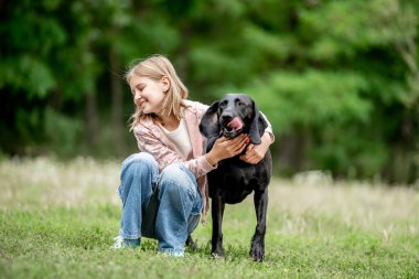 Golden Retriever köpeğini kucaklayan küçük kız doğada birlikte oturuyor. Sevimli çocuk yazın parkta safkan köpek labrador 'u besliyor.