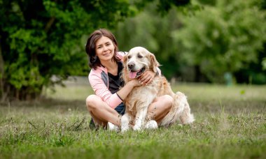 Golden Retriever köpeğini kucaklayan güzel bir kız doğada çimlerde oturuyor. Yazın parkta safkan evcil köpek labrador 'u olan güzel bir genç kadın.