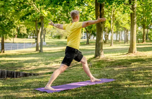 Man practicing yoga standing on mat outdoors at summer. Guy doing pilates workout for stretching muscles