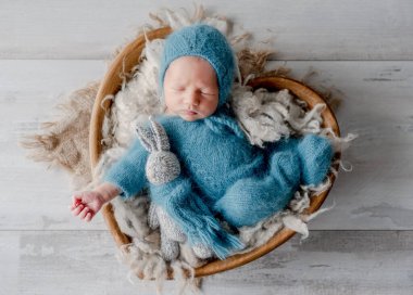 Sevimli yeni doğmuş bebek elinde kalp şeklinde sepet şeklinde stüdyo resminde örülmüş tavşan oyuncağı tutarak uyuyor. Sevimli çocuk uyuyor.