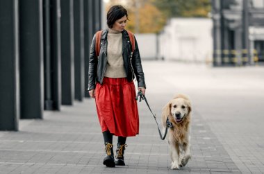 Sokakta yürüyen genç bir kadın Golden Retriever köpeğiyle