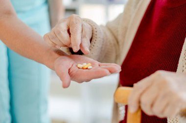 Hemşire eli, yaşlı bir kadının yakın çekimde aldığı hapları tutuyor.