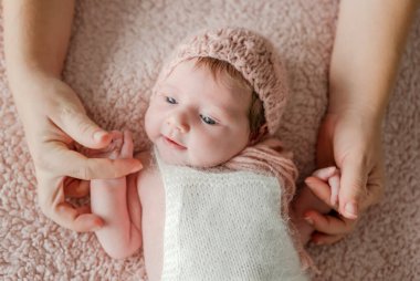 Çiçek çelenk takan yeni doğmuş bebek uyuyor ve annesi elini tutuyor. Bebeklerin uyuması, ebeveynlerin bakımı ve sevgisi