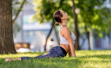 Doğada yoga yapan ve yukarı doğru köpek pozu veren bir kız. Genç bir kadın yazın egzersiz yapıyor ve kısırlaştırıyor.