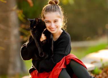 Güz yaprakları portresiyle sokakta siyah kediye sarılan güzel bir kız. Güz mevsiminde parkta kedisi olan güzel bir genç.