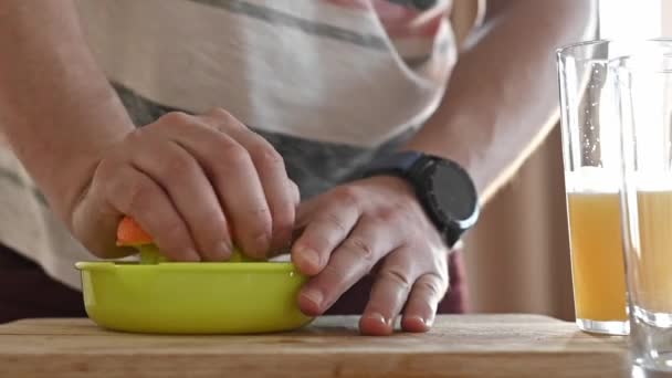 人の手は台所で自然なジュースを作るための手動抽出器で熟したオレンジを絞る 家で柑橘類からトロピカルフルーツドリンクを準備する男 — ストック動画