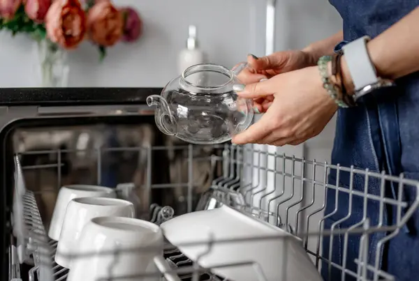 女人们手握透明茶壶 相对于洗碗机 整理干净的餐具 — 图库照片
