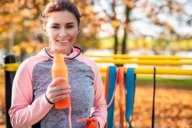 Sonbahar parkında egzersiz yaptıktan sonra şişeli fitness kızı. Genç kadın ve hidrasyon sporunun sonbahar portresi