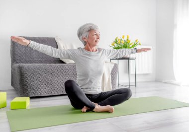 Parlak bir odada sakin ev egzersizleri, 70 yaşında bir kadın yoga yapıyor.