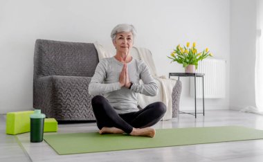 Parlak bir odada sakin ev egzersizleri, 70 yaşında bir kadın yoga yapıyor.