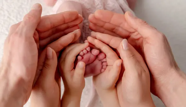 Mom, Dad, And Older SisterS Hands Hold NewbornS Feet In An Artistic Photo