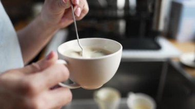 Girl hand stiring coffee cappuccino in cup at kitchen for breakfast. Morning espressoo latte beverage at home