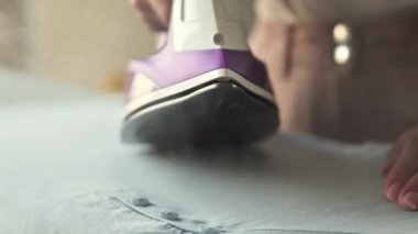 Kırışık giysiler için buhar modunda demir kullanan kız eli, yakın görüş. Ateşli elektrikli aletli bir kadın tekstili düzeltiyor.