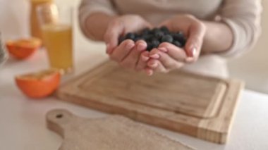 Girl holding in hands blueberry at kitchen with natural orange juice. Woman with berries and tropical citrus fruits at home