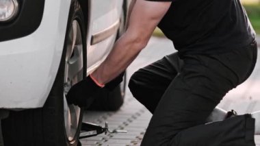 Tamirci, Wrench ile tekerlek cıvatasını sökmek için özenle çalışıyor.