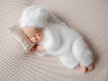 Newborn Baby In White Jumpsuit Sleeps During Studio Photoshoot clipart