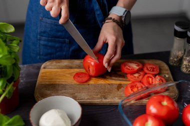 Kadın elleri Mozzarella 'nın yanındaki tahtada domatesleri kesiyor.