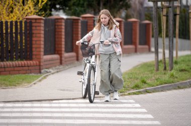 Kız baharda yaya geçidinde bisikletle karşıya geçiyor.