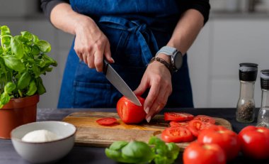 Caprese Salatası 'nı hazırlamak, Kadın Elleri, Mozzarella, Basil ve Baharatlar ile birlikte bir tahtada domates kesiyor.