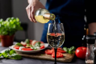 KADIN Elleri, Caprese Salatası 'nın arka planına karşı bardağa şarap döker.