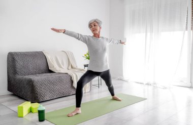 Parlak bir odada sakin ev egzersizleri, 70 yaşında bir kadın yoga yapıyor.