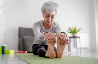 Emeklilikte spor yaşam tarzı, oturma odasının zemininde tatlı gri saçlı bir kadın egzersiz yapıyor.