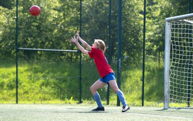 Kız kaleci çocuklar futbol maçında topu yakalamaya çalışıyor.