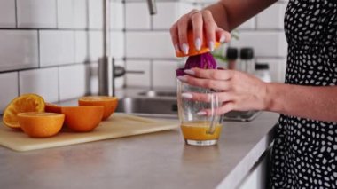 Kadın evde, mutfakta portakal suyu yapıyor.