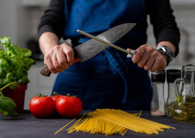 Büyük mutfak bıçağı ve keskinleştirici masanda spagetti, domates, baharat ve fesleğen var.
