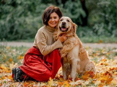 Sonbahar parkında Golden Retriever köpeğiyle genç bir kadın.