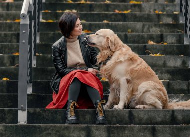 Genç bir kadın merdivende oturuyor ve Golden Retriever köpeğini okşuyor