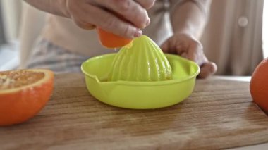 Girl hand squeeze ripe orange to manual extractor for making natural juice at kitchen. Woman preparing tropical fruit drink at home