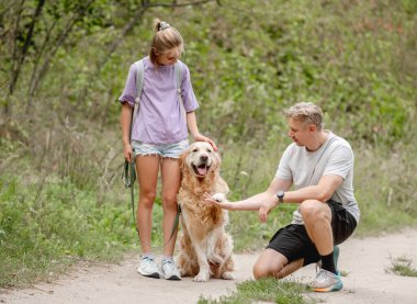 Kızım ve babam, mutlu bir şekilde altın av köpeğine bir yaz günü pençe atmayı öğretiyor.