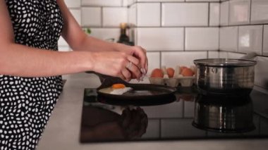 Kızarmış tavaya yumurta kıran ve çırpılmış yumurta pişiren bir kız.