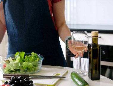 Genç kadın evde, mutfakta Yunan salatasını hazırlarken, ev yemeklerini kucaklarken beyaz şaraptan hoşlanıyor.