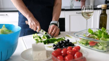 Kadın Elleri, Yunan salatası için bir bardak beyaz şarapla salatalık dilimliyor