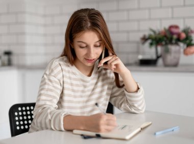 Genç kız telefonda konuşuyor ve evdeki not defterine notlar yazıyor.