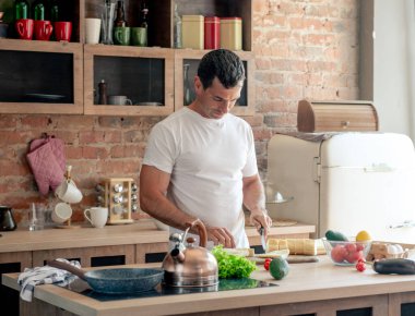 Çekici atletik adam mutfakta taze ekmek kesiyor, sağlıklı ve sportif bir kahvaltı hazırlıyor.