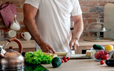 Atletik Adam, mutfakta sağlıklı bir kahvaltı için kesme tahtasıyla peynir kesiyor.