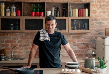 Çekici atletik adam mutfakta yemek pişirdikten ve temizlik yaptıktan sonra kameraya bakarken gülümsüyor.