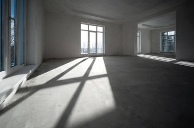 Büyük, aydınlık ve büyük pencerelerden içeri ışık huzmeleri giren boş bir salonda.