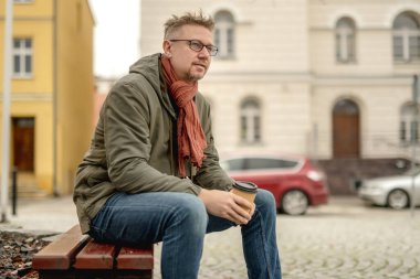 Genç Çekici Adam parkta oturur, kahve içer ve bekler.