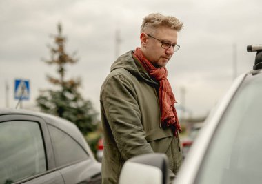 Çekici genç bir adam sokağa bir araba park eder ve kapıyı açarak arabaya biner.