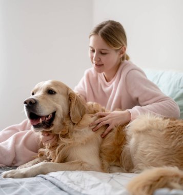 Sevimli küçük kız neşe içinde yatakta güzel bir köpekle oynuyor.