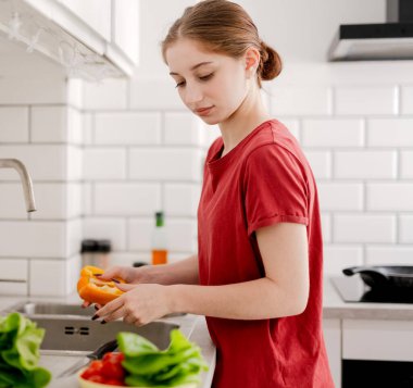 Ev Mutfağında biber yıkayan genç kız.